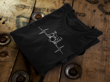 Load image into Gallery viewer, Rhythmic Pulse Tee neatly folded on a wooden spool, highlighting the drummer&#39;s heartbeat design against the rich, natural backdrop.